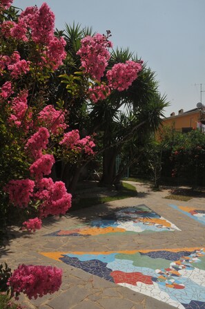 Un chemin pavé orné de mosaïques colorées, bordé d’une végétation luxuriante et d’arbres à fleurs roses.