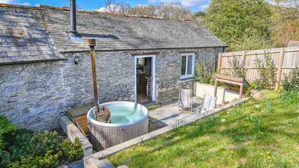 A stone house with a hot tub, wooden deck, and a wooden fence. - Award winning stunning barn conversion over looking nature reserve (Landulph)