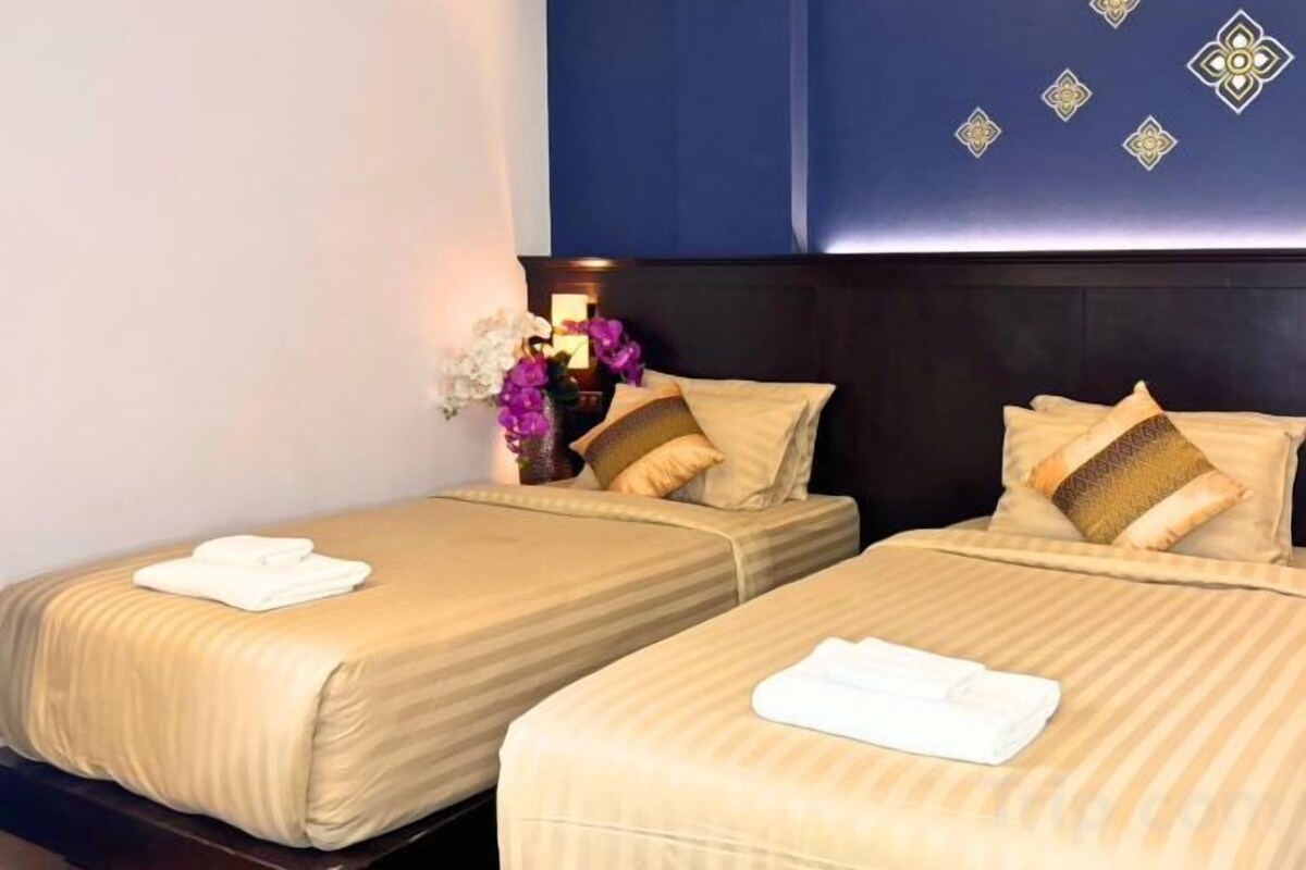 Une chambre d’hôtel avec deux lits, chacun agrémenté d’une serviette blanche soigneusement pliée, d’un vase avec des fleurs et d’une tête de lit sombre ornée de motifs décoratifs.