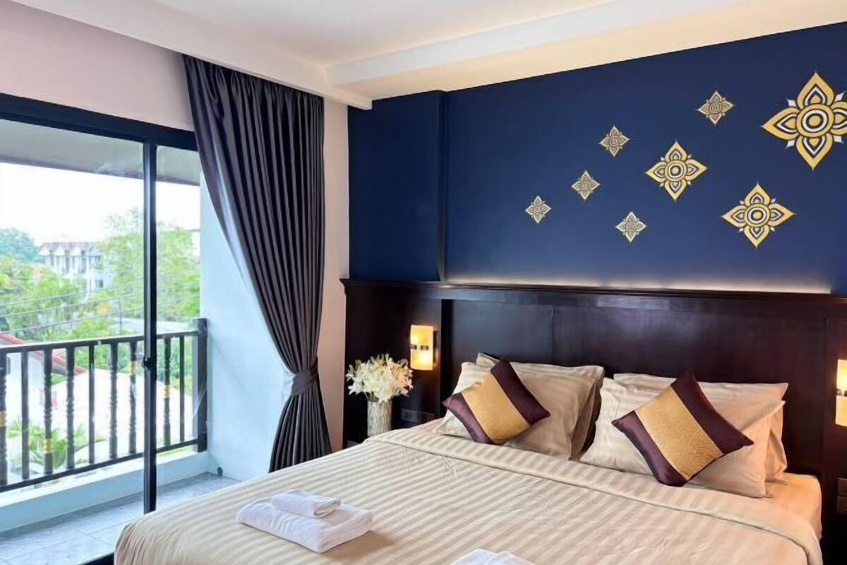 Een hotelkamer met een groot bed, een balkon met gordijnen en decoratieve muurpatronen.