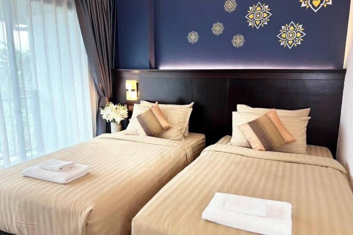Een hotelkamer met twee bedden, een donker hoofdeinde en decoratieve wandmotieven.