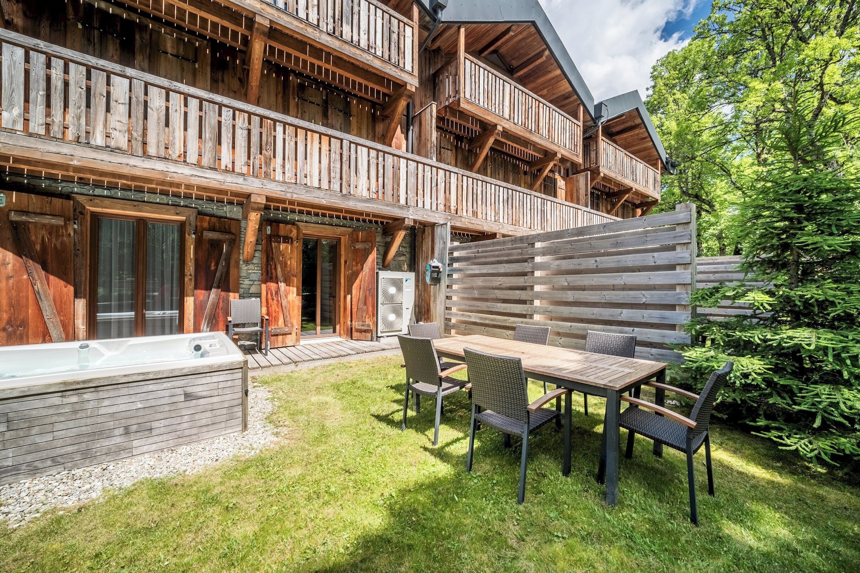 Un chalet in legno con un balcone, una vasca idromassaggio e un patio con tavolo e sedie.