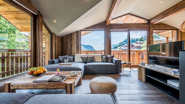 A modern living room with a large sofa, a coffee table with fruits, and a TV. - MOULIN III - Luxury chalet with private hot tub (Les Gets)