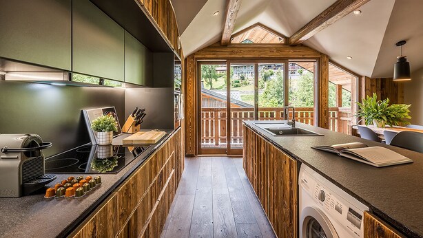 A modern kitchen with wooden accents, a built-in oven, and a large window overlooking a deck. - MOULIN II - Design chalet with private hot-tub (Les Gets)