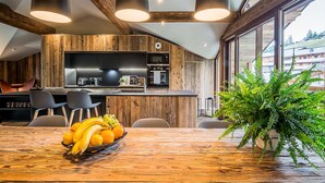 A modern kitchen with wooden accents, a dining area with a fruit bowl, and large windows. - MOULIN II - Design chalet with private hot-tub (Les Gets)