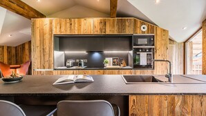 A modern kitchen with wooden accents, built-in appliances, and a central island with seating. - MOULIN II - Design chalet with private hot-tub (Les Gets)