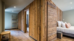 A bedroom with a wooden partition, a bed with pillows, a bedside table, and a ladder in the corner. - MOULIN II - Design chalet with private hot-tub (Les Gets)