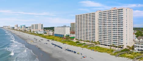 A beachfront hotel with multiple floors, a sandy beach, and a clear view of the ocean.