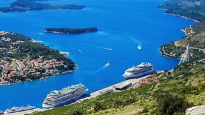 A coastal town with a cruise ship docked at a pier, surrounded by lush greenery and clear blue waters. - ORA Luxury Rooms (Dubrovnik)