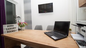 A modern office space with a wooden desk, a laptop, a sign reading "#ORA LUXURY ROOMS", a potted plant, a TV on the wall, and a printer. - ORA Luxury Rooms (Dubrovnik)