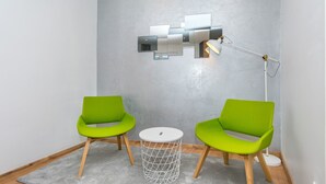 A modern room with two green chairs, a small white table, and a unique wall-mounted light fixture. - ORA Luxury Rooms (Dubrovnik)