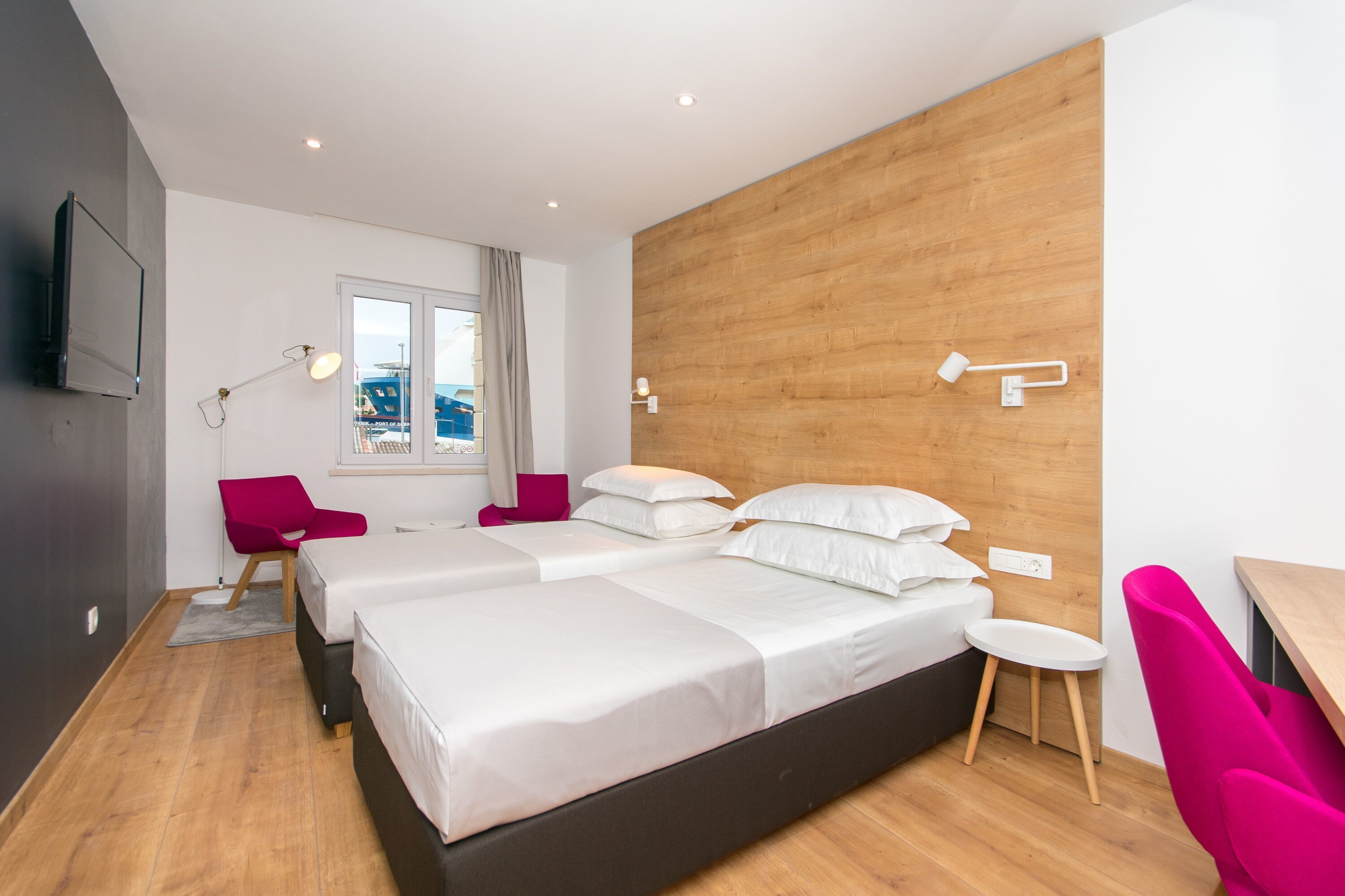 Habitación de hotel moderna con dos camas, un escritorio, una silla y ventana con vista a la ciudad.