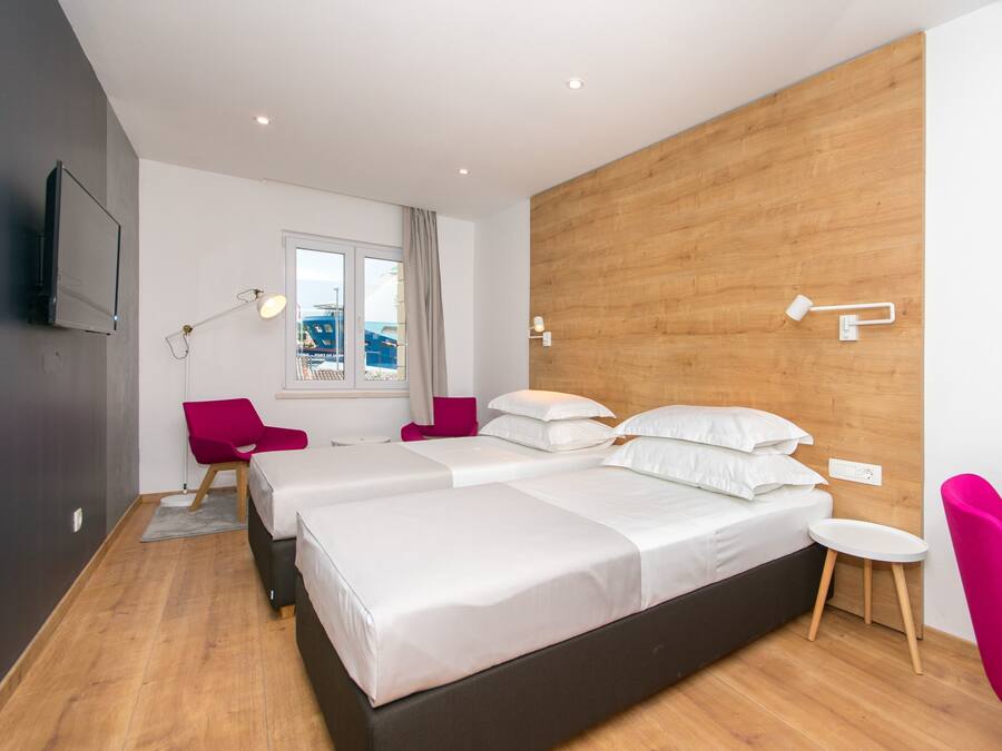 Habitación de hotel moderna con dos camas, un escritorio, una silla y ventana con vista a la ciudad.