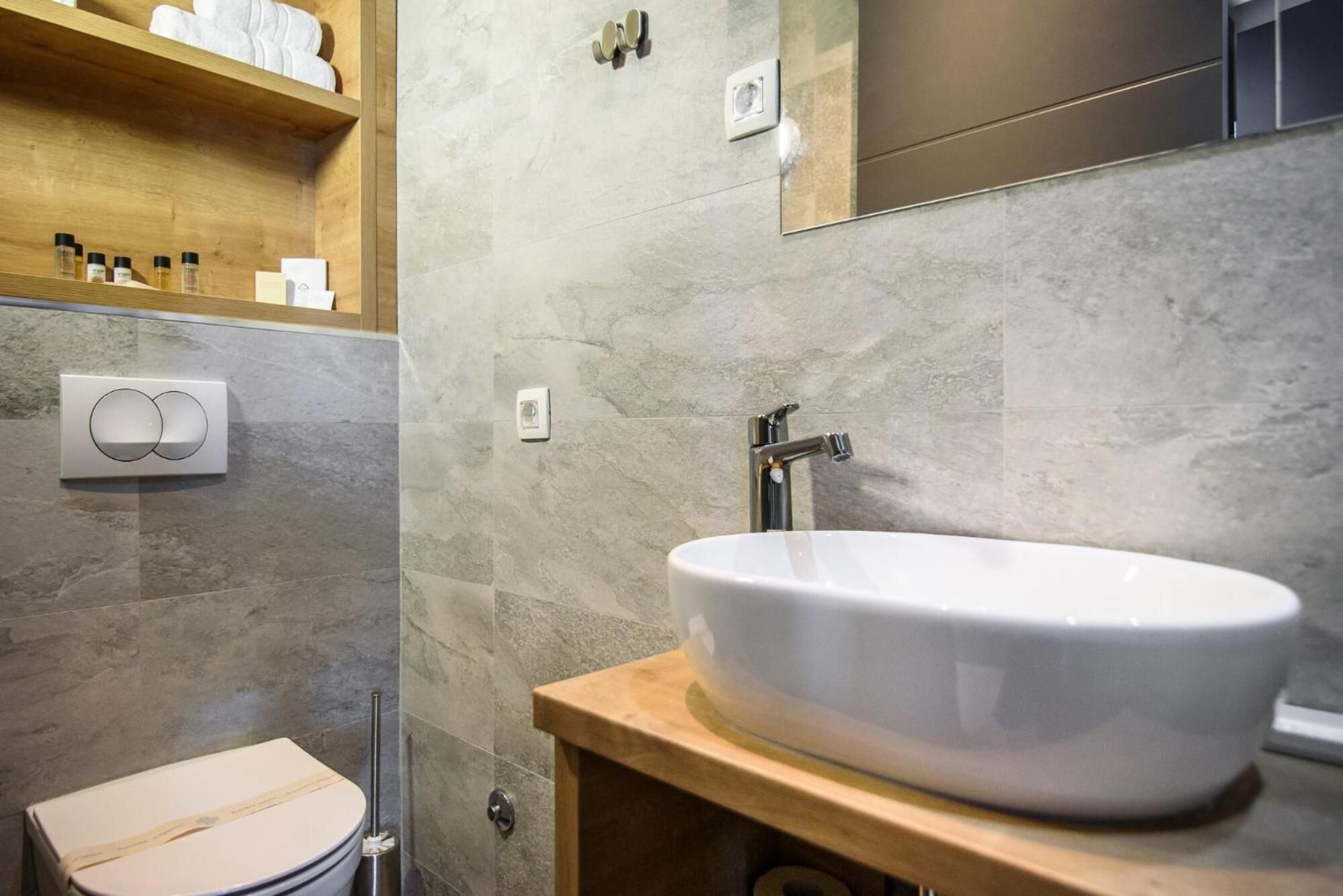 Un baño con un lavamanos blanco, estantes de madera y un inodoro.