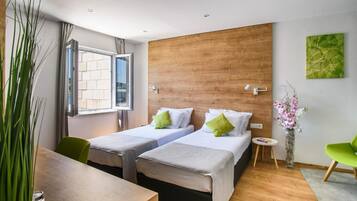 Une chambre d’hôtel moderne avec deux lits, un mur décoratif en bois, une grande fenêtre et un fauteuil vert.