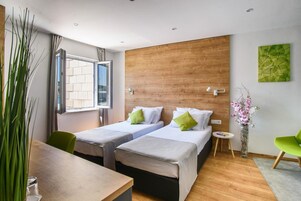 Quarto de hotel moderno com duas camas, um painel de madeira decorativo, uma janela grande e uma cadeira verde.