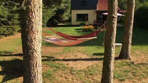 A hammock between trees in a grassy area with a house in the background. - Ferienhaus Mirow-Lärz - Kamin Wald Ruhe (Laerz)