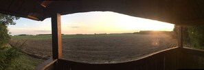 A view from a covered area with a dirt field in the foreground and a sunset in the background. - Ferienhaus Mirow-Lärz - Kamin Wald Ruhe (Laerz)