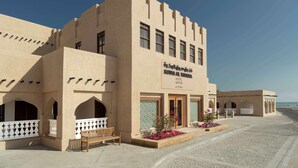A hotel with a beige facade, multiple windows, and a sign indicating it is located in Qatar. - Souq Al Wakra Hotel Qatar by Tivoli (Al Wakrah)
