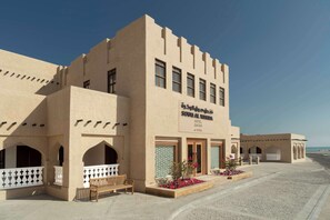 A hotel with a beige facade, multiple windows, and a sign indicating it is located in Qatar. - Souq Al Wakra Hotel Qatar by Tivoli (Al Wakrah)
