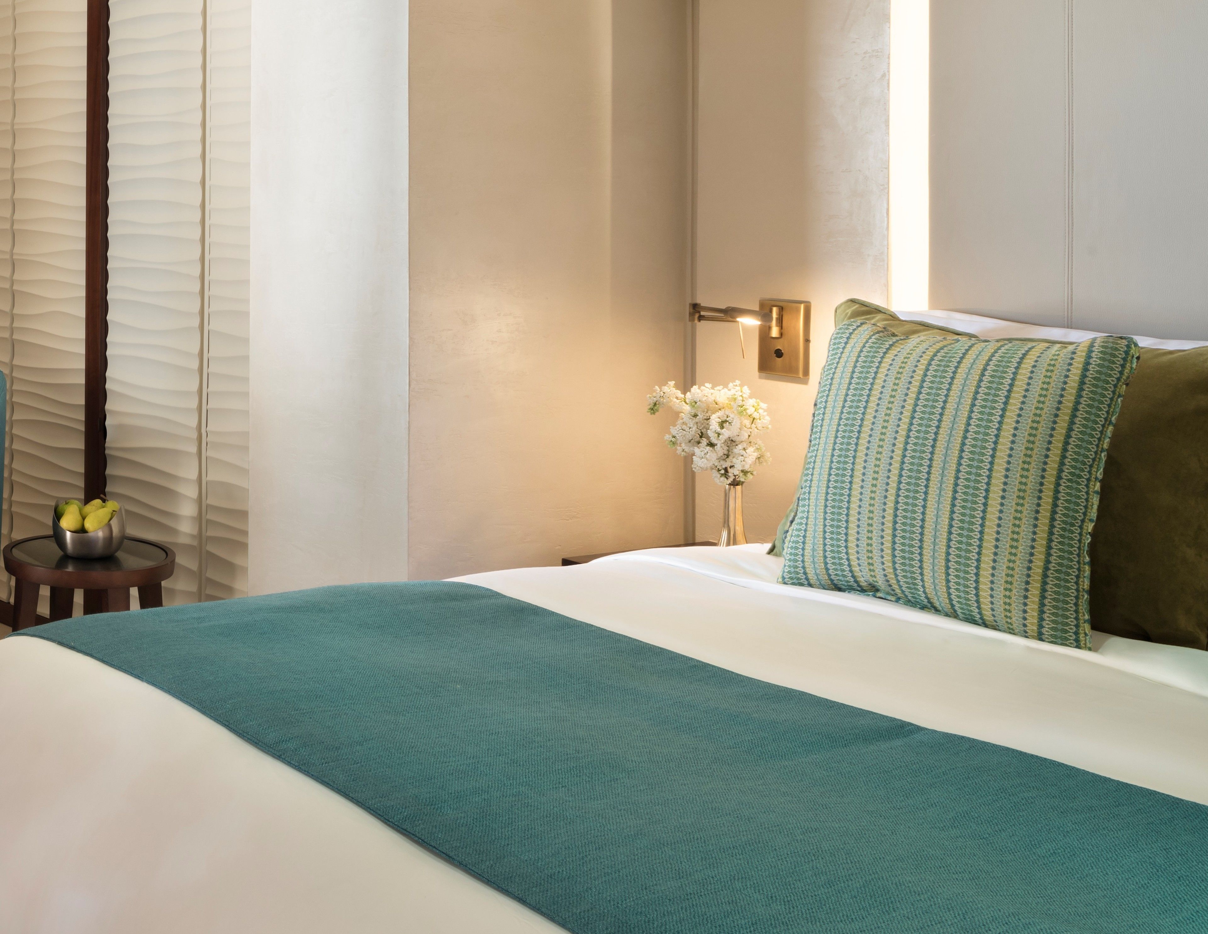 Habitación de hotel con cama, mesita de noche, un jarrón de flores y ventana con cortinas.
