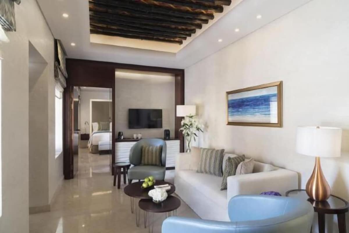 A hotel room with a living area, a sofa, a coffee table, a TV, and a painting on the wall.