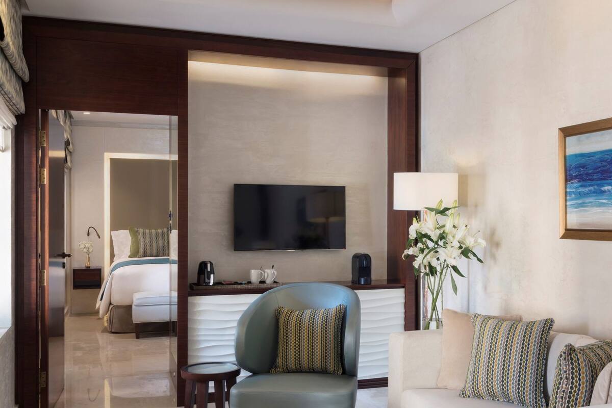 A hotel room with a bed, a TV, a coffee maker, a chair, a sofa, and a painting.