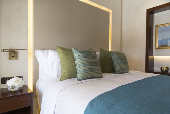 A neatly made bed with white and green pillows, a blue throw blanket, and a wooden headboard.