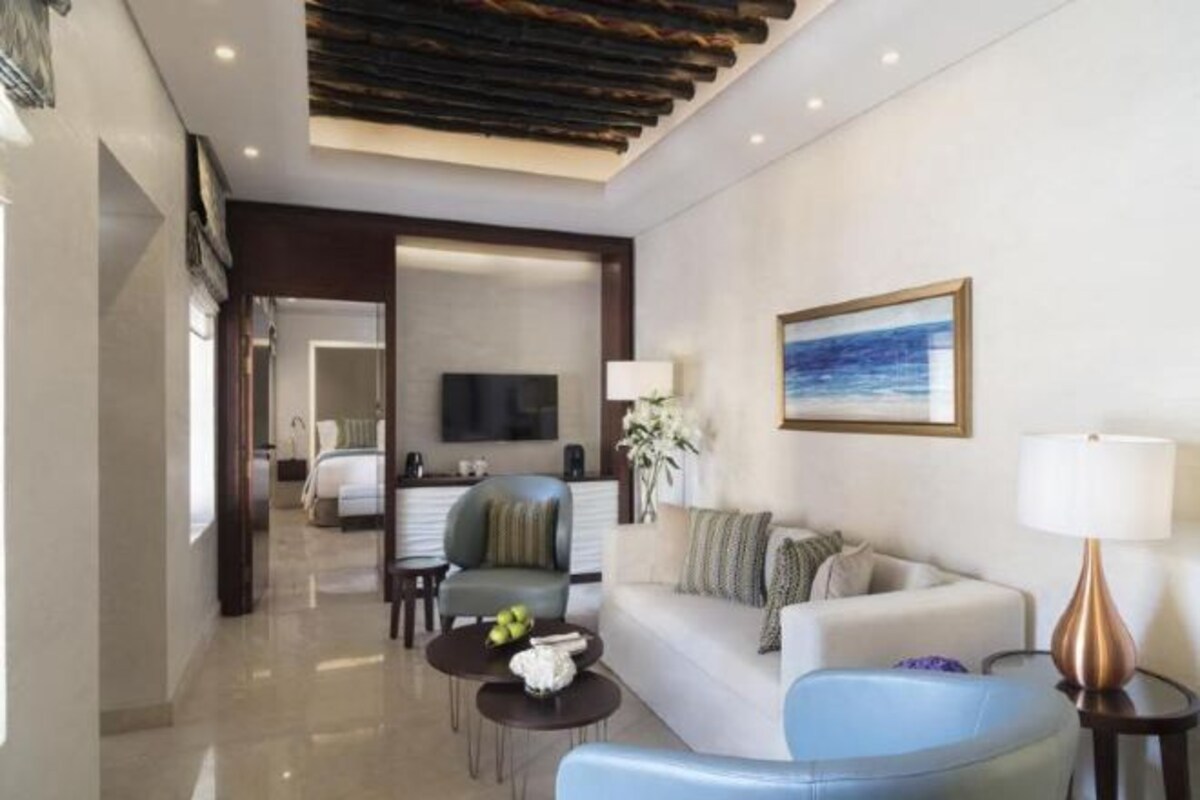 A hotel room with a living area, a sofa, a coffee table, a TV, and a painting on the wall.