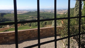 A view through a window with a stone wall and gravel ground, overlooking a landscape with fields and distant hills. - Il Burellino Wine & Resort (Montalcino)