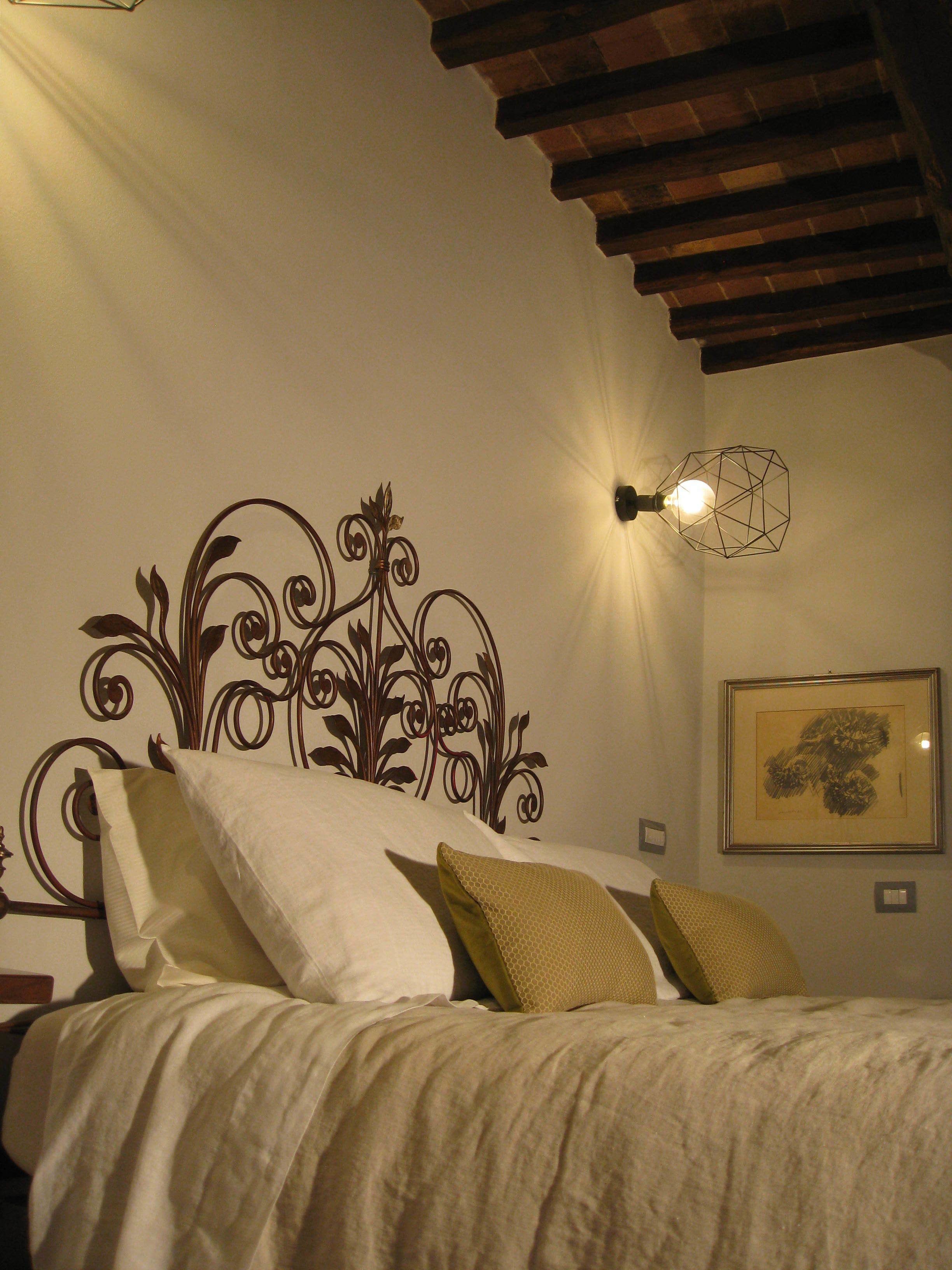 A bedroom with a decorative headboard, a wall-mounted light fixture, and a framed picture on the wall.