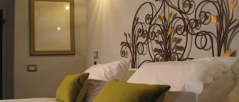 A neatly made bed with white linens and two green pillows, a wall-mounted light fixture, and a decorative metal wall art piece.