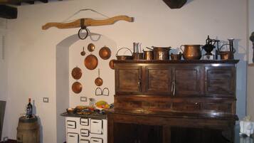 A kitchen with a wooden cabinet, a vintage stove, and various kitchen utensils hanging on the wall.