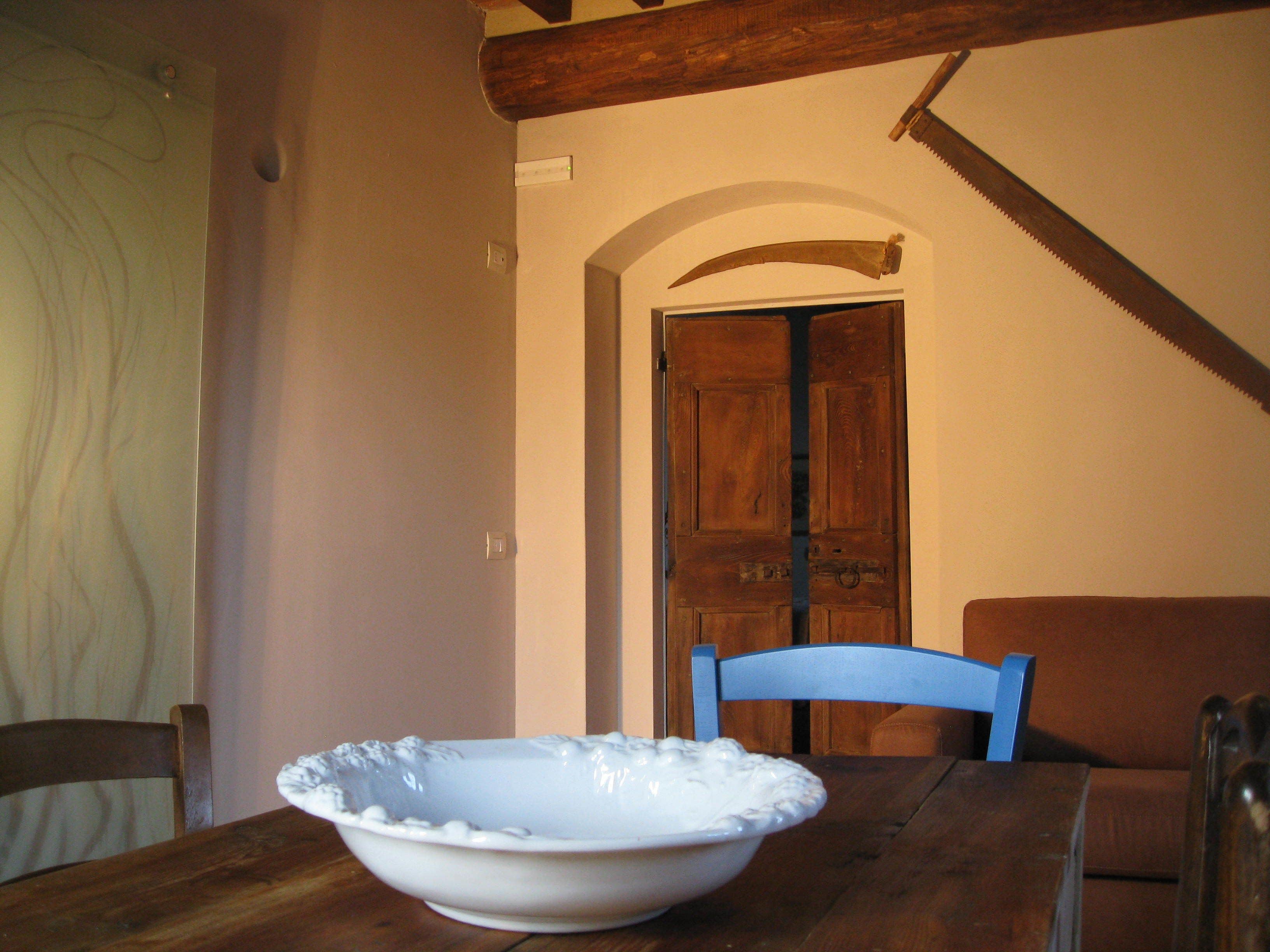 A dining table with a white bowl, a wooden chair, and a wooden door in the background.