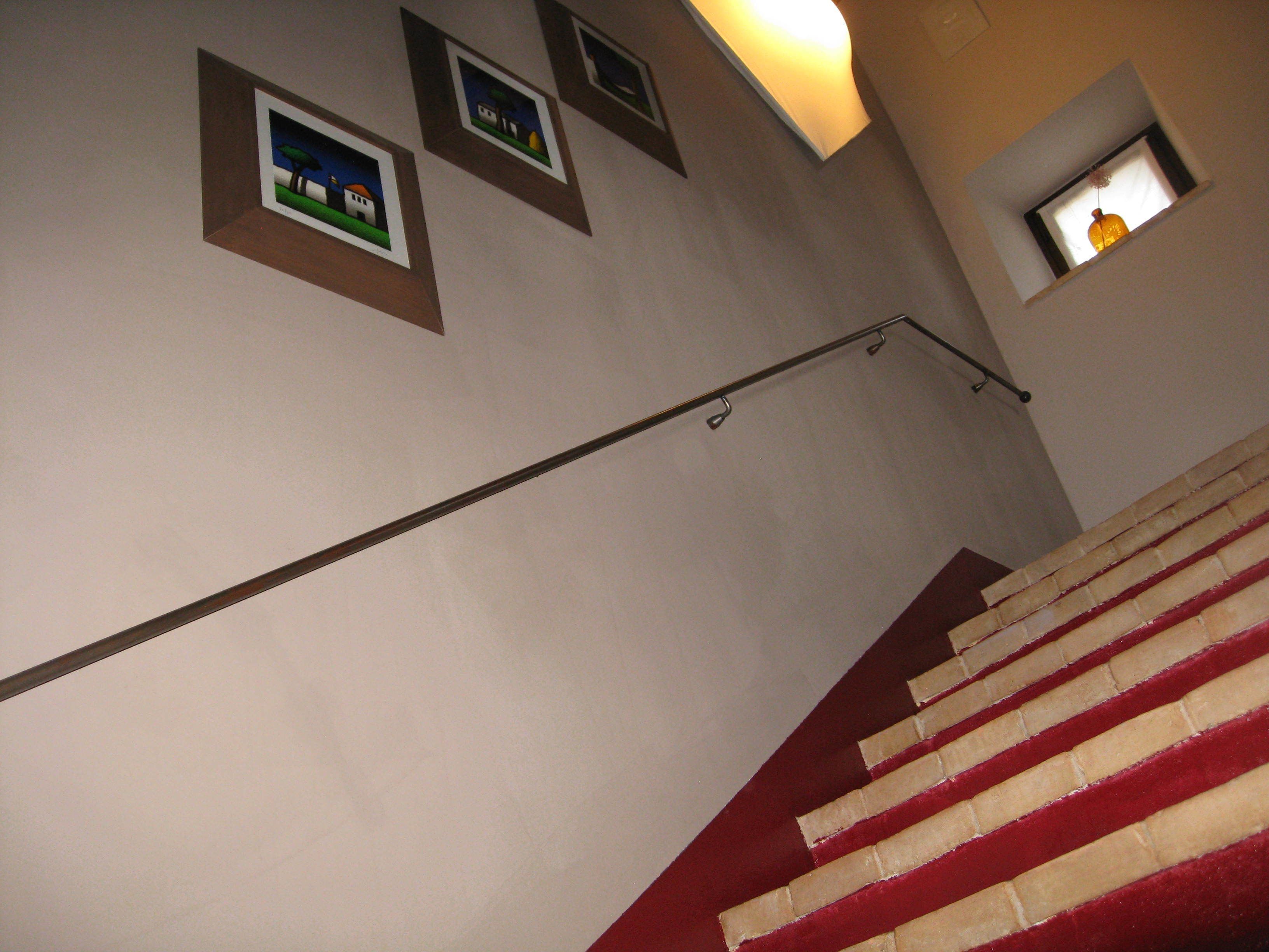 A staircase with red and white steps leading upwards, a handrail, and three framed pictures on the wall.