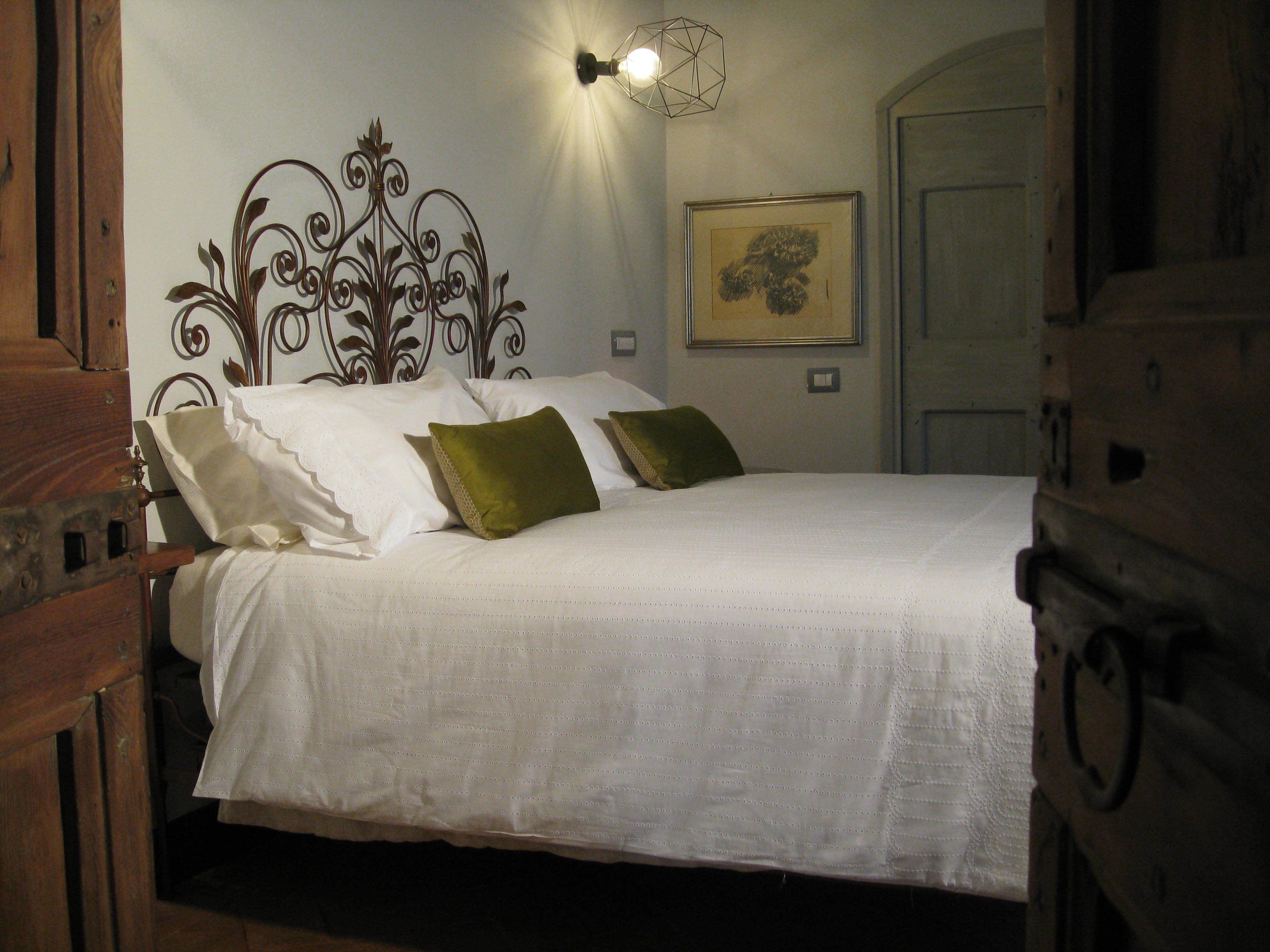 A neatly made bed with white linens and two green pillows, a decorative wall sconce, and a framed artwork above the bed.