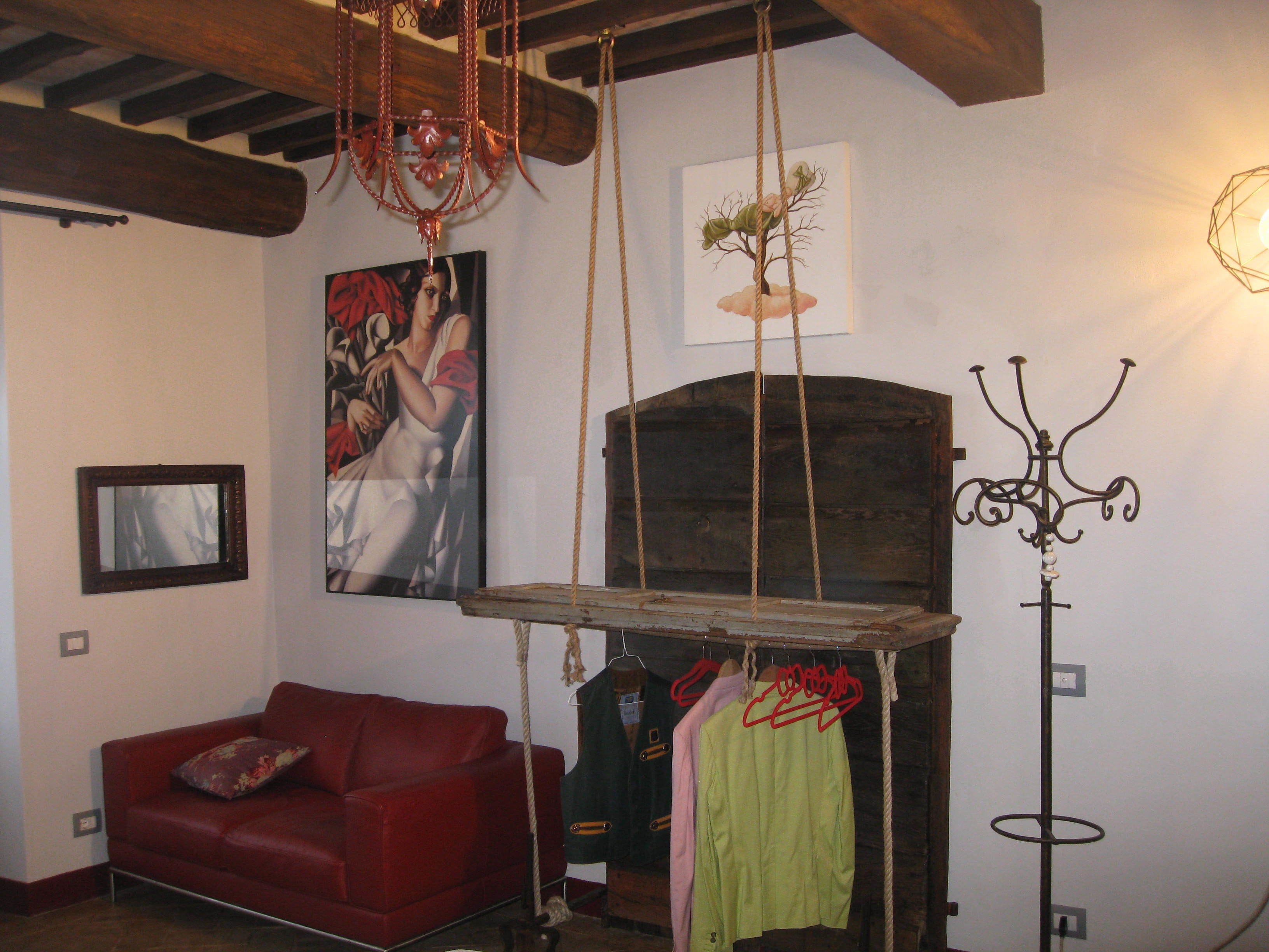 A room with a red sofa, a painting, a wooden beam ceiling, and a hanging coat rack.