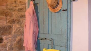 Une porte rustique ornée d’un chapeau tressé, un vêtement rose accroché à un crochet et une chaise jaune.