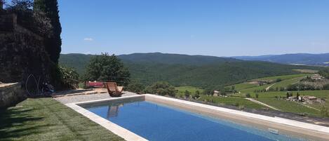 A swimming pool with a clear view of the surrounding landscape, including hills and vineyards.