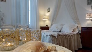 Un dormitorio con cama a dosel, lámparas de noche, una mesita de noche y objetos decorativos como velas y caracolas.
