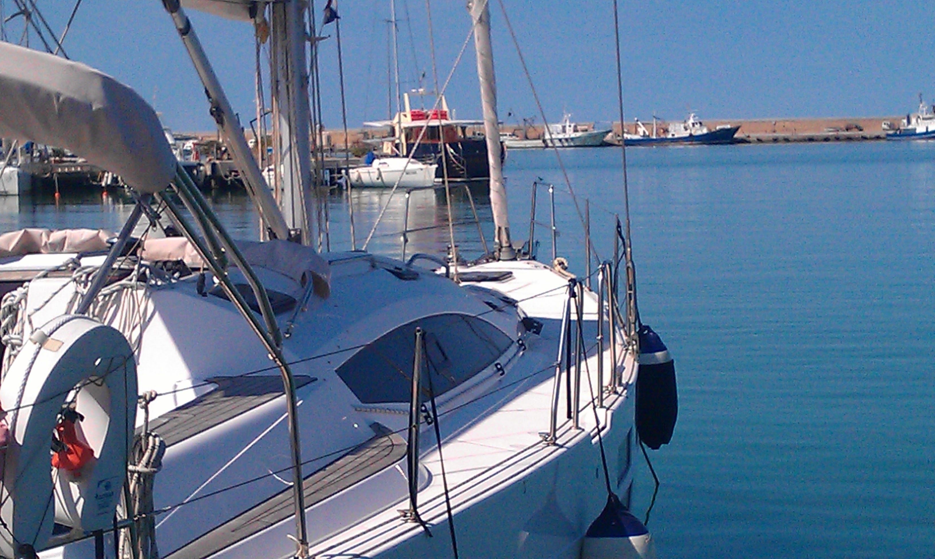A sailboat docked at a marina with calm water and other boats in the background.