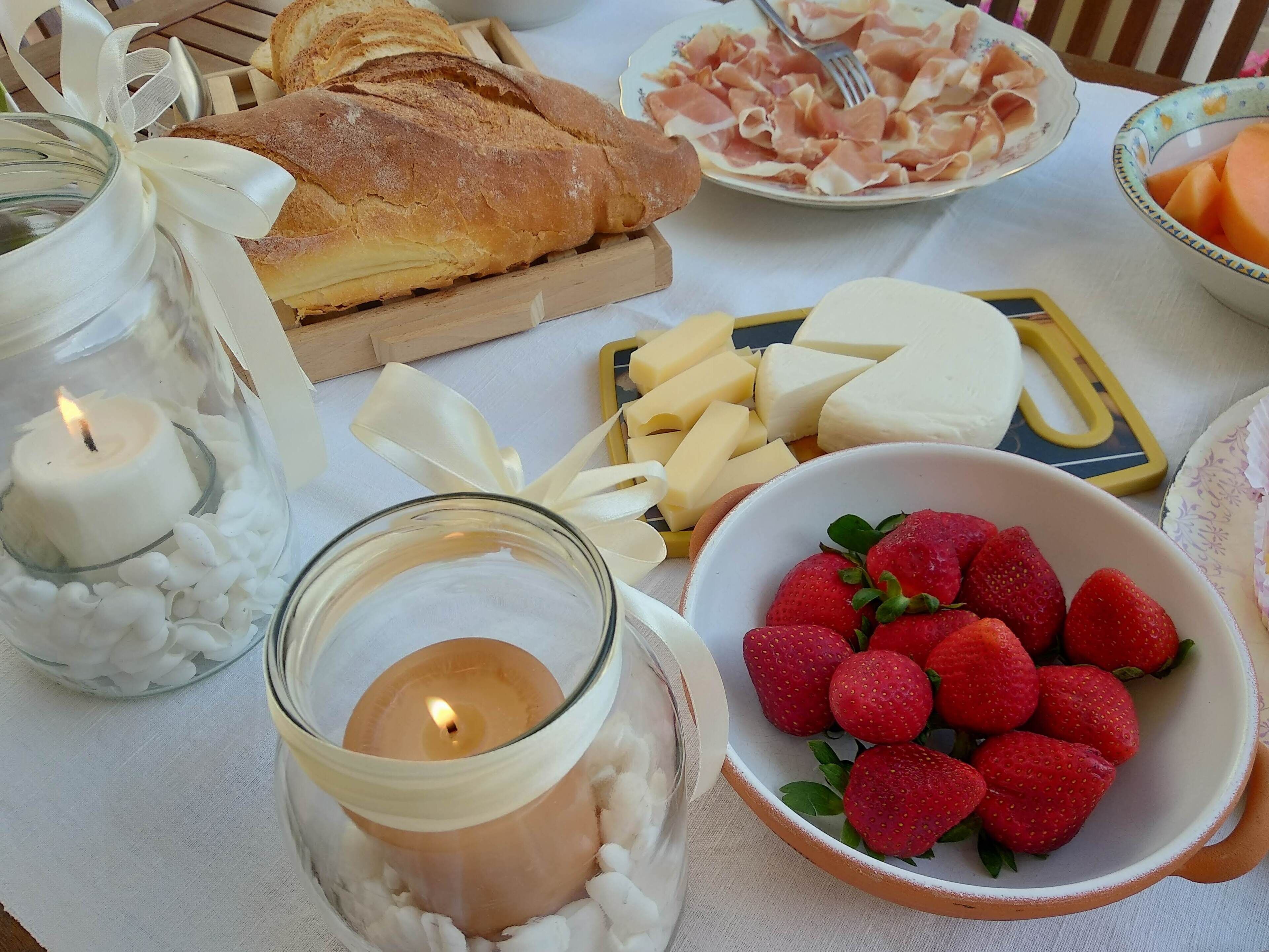 Une table avec une miche de pain, du fromage, des fraises et une bougie.