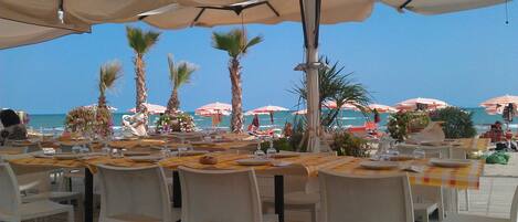 An outdoor dining area with tables and chairs, overlooking the beach.