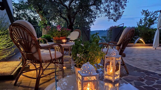 Un espacio al aire libre con sillas de mimbre, una mesa de vidrio y dos faroles iluminados.