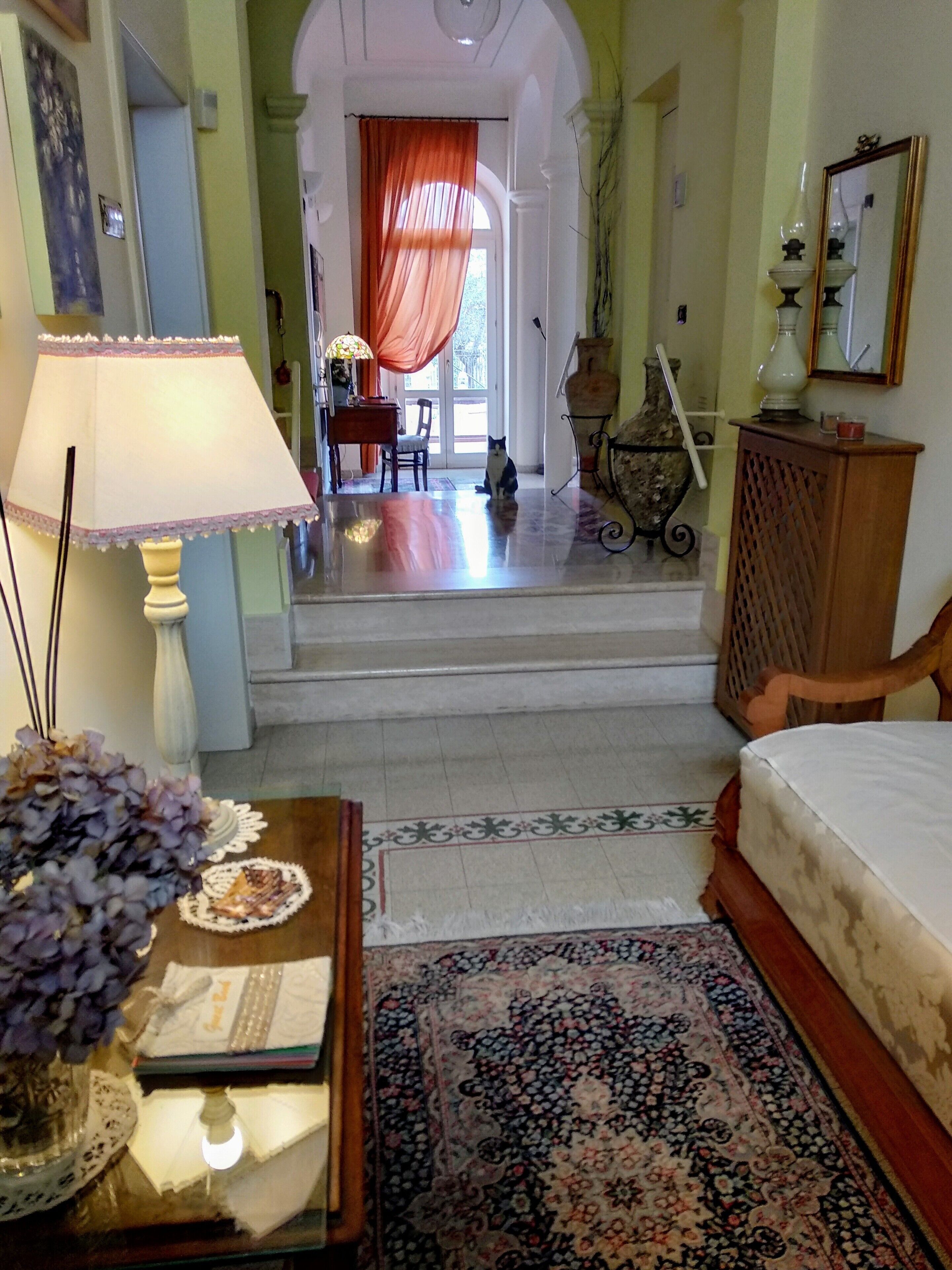 Una habitación con cama, lámpara, un jarrón con flores, alfombra y vistas a un comedor con mesa y sillas.