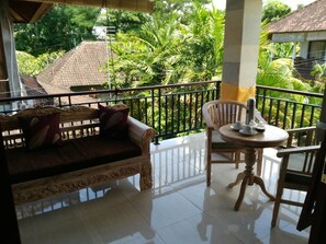 A balcony with a wooden sofa and a small table, surrounded by a metal railing. - Qiul Guest House (Ubud)