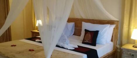 A bedroom with a four-poster canopy bed, wooden headboard, bedside tables, and a nightstand with a lamp.