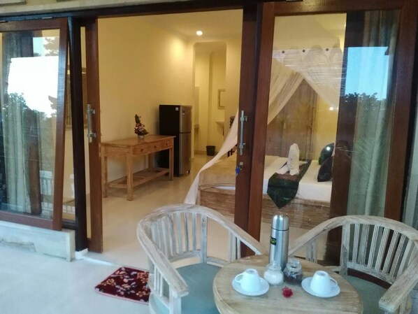 A room with a dining area featuring a round table with chairs, a refrigerator, and a bed with a canopy. - Qiul Guest House (Ubud)