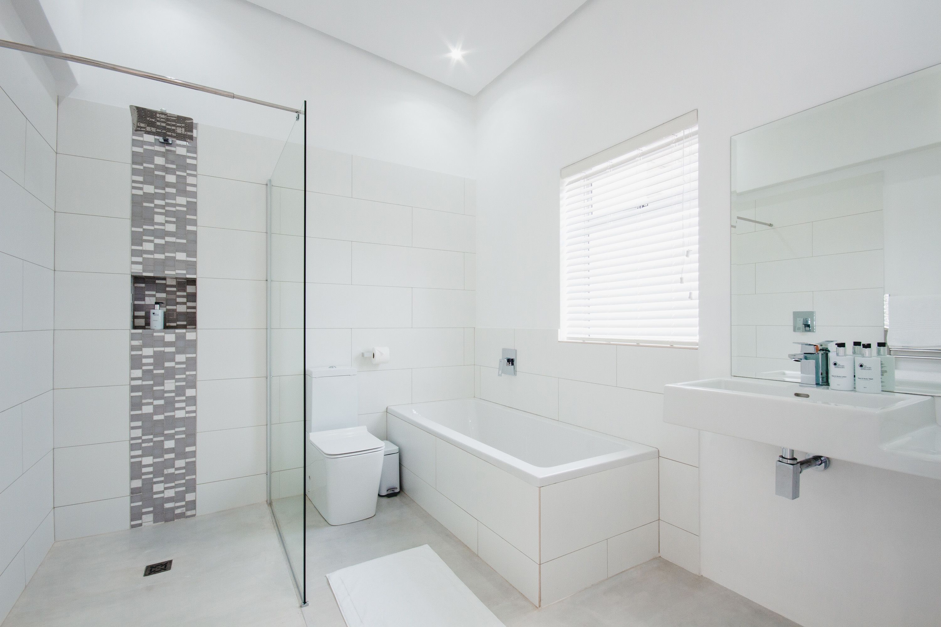 A modern bathroom with a glass shower enclosure, a white bathtub, and a large mirror above the sink.