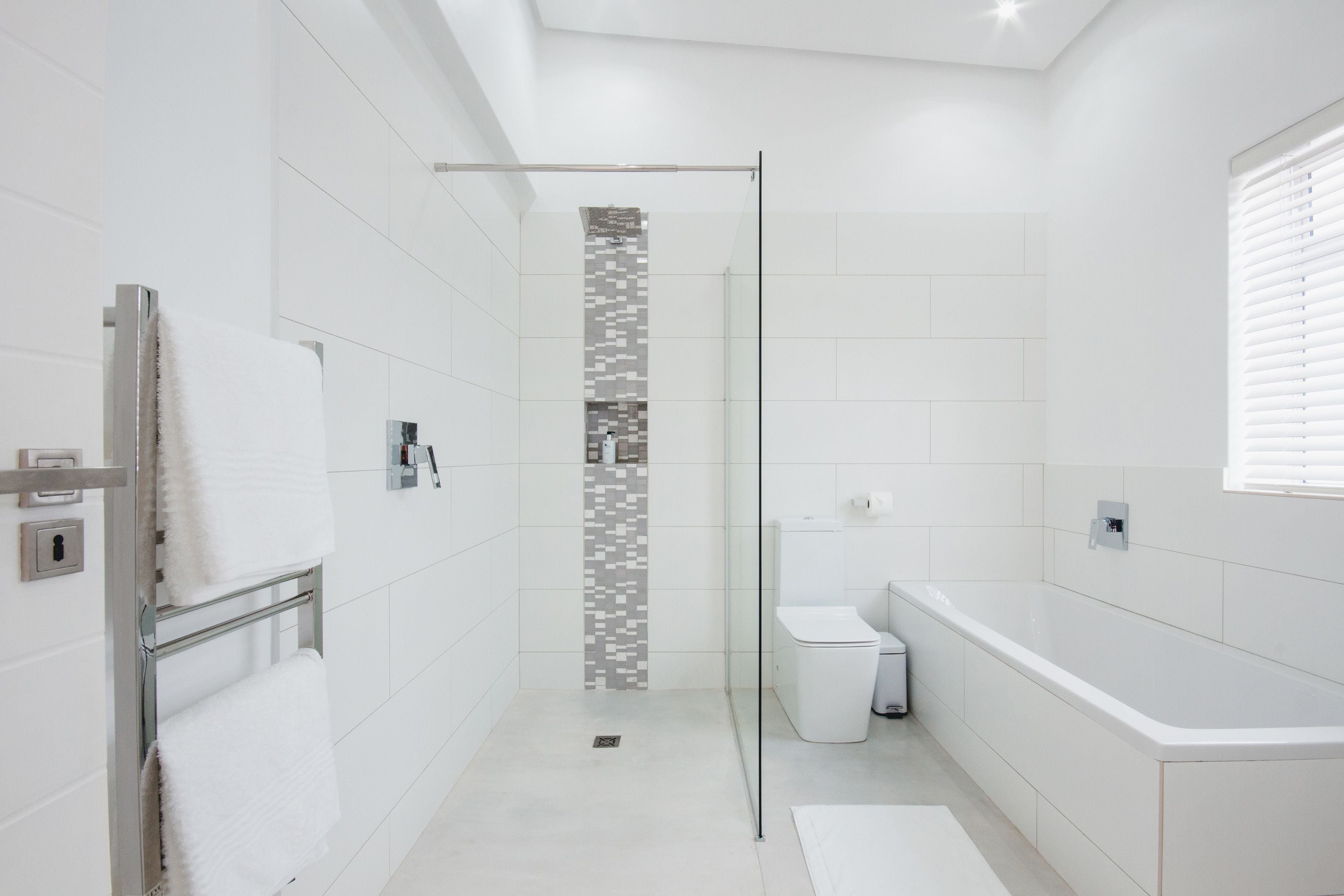 A modern bathroom with a glass-enclosed shower, white tiles, a toilet, and a bathtub.